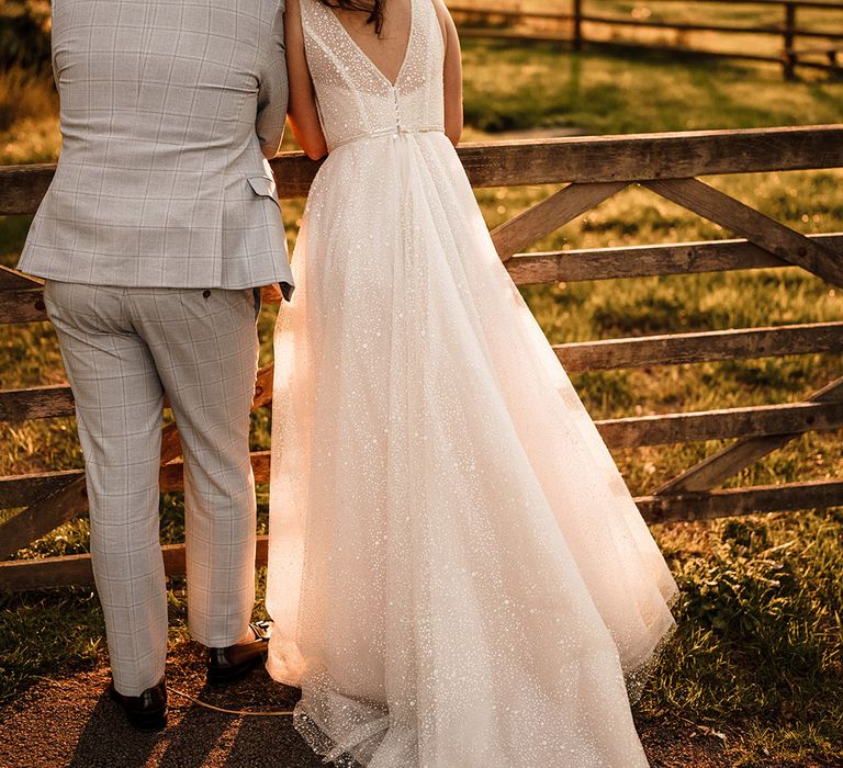 Bride in a sparkly princess wedding dress by Gabbiano and groom in a light blue suit looking over a stone wall during golden hour 