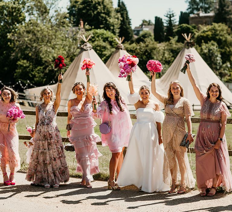 Bridesmaids in pink mismatched bridesmaid dresses with pink bouquets standing with the bride in front of the tipi wedding 