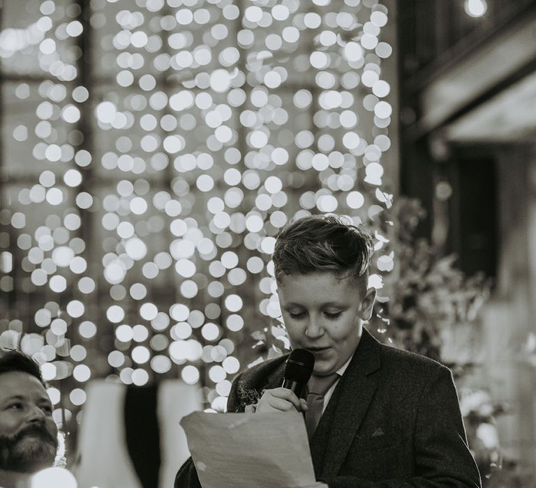 The bride and groom's son performs a wedding speech with fairy lights in the background 