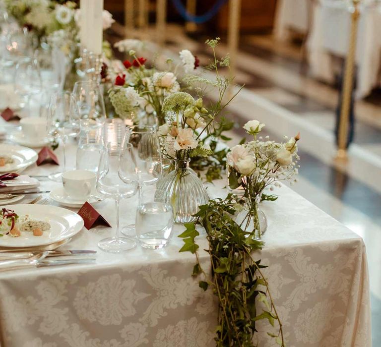 Classic wedding tablescape at Inner Temple Hall with white tapered candles in gold candelabras, red wedding table names, white rose, baby's-breath and foliage wedding centrepieces and foliage table runners