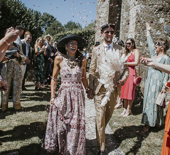 Bride in boho pink wedding dress and groom in pinstripe suit leave church ceremony with a confetti exit