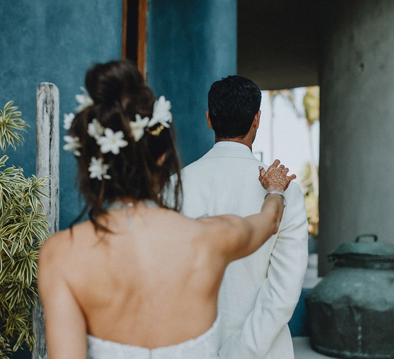 Bride with flower hair accessories taps groom in cream groom suit on the shoulder during first look photos