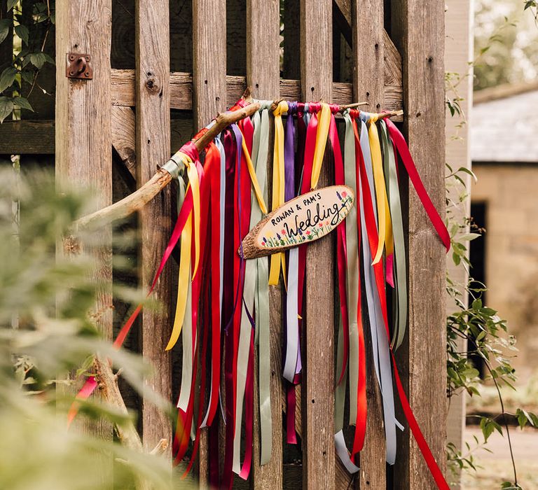 Rainbow coloured ribbons hang with DIY wood slice wedding sign 