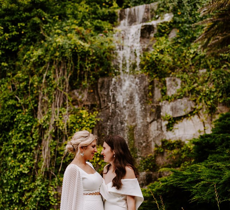 Couple portrait of two brides wearing white wedding gown and two piece with pastel bouquet