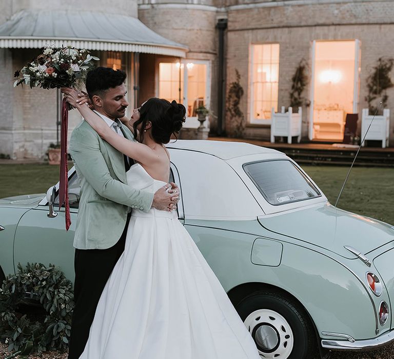 Mint green 1991 Nissan Figaro wedding car with the bride and groom embracing in front of the car 