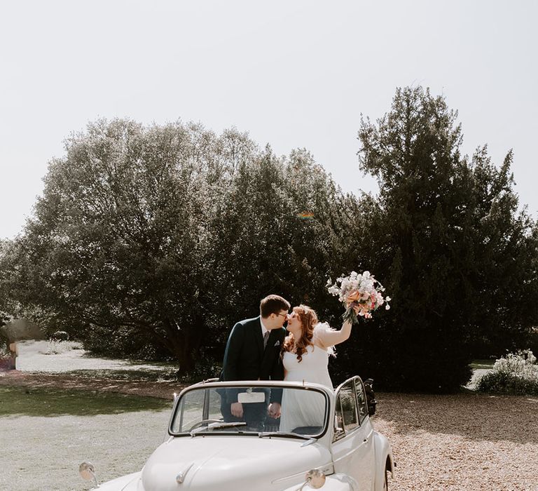 White wedding car transportation for the Preston Court wedding with the bride and groom standing in the back posing together 