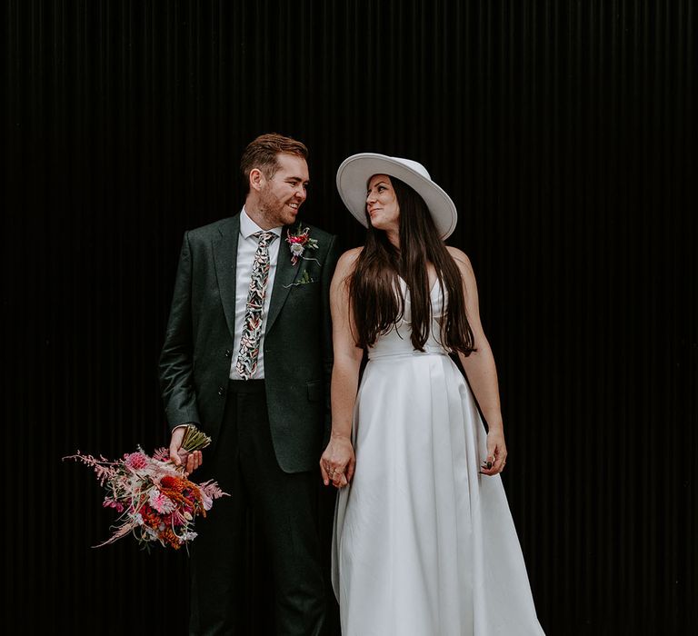 Groom in dark green suit with the bride in a white wedding dress and bridal hat 