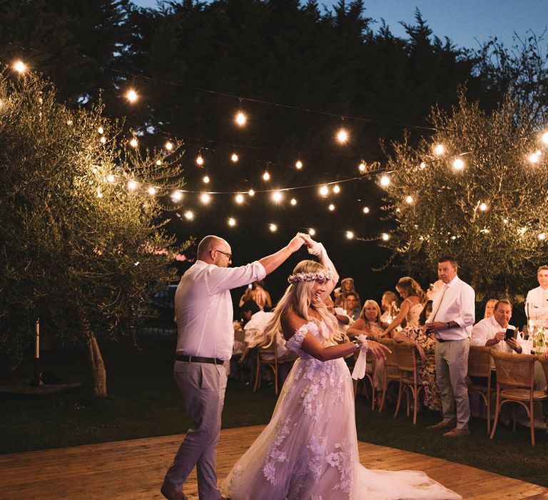 Bride and groom have their first dance together on the outdoor dance floor with festoon lighting 