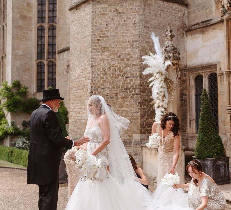 Bridesmaids in gold sequin dresses with father of the bride in a top hat helping the bride on the way to the wedding 