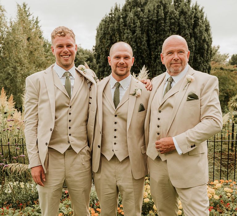 The groom and groomsmen wearing beige three piece wedding suits with green satin tie and pocket square 