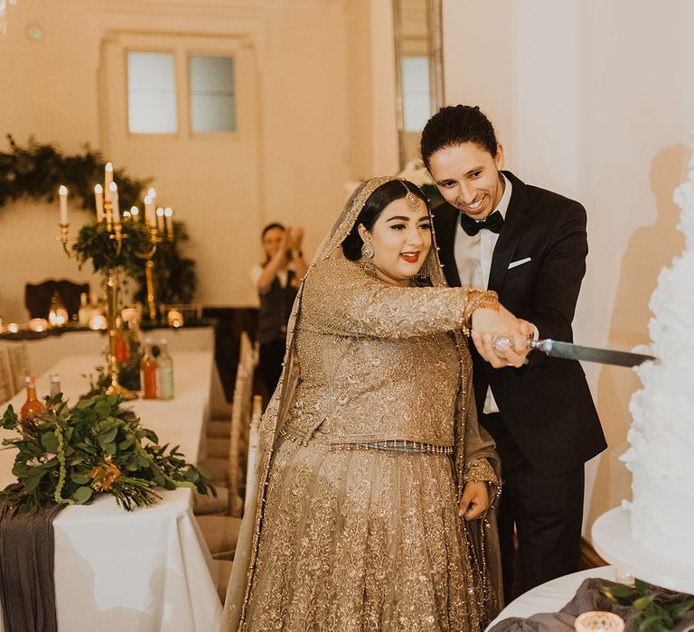 Bride in a  gold wedding dress and groom in a tuxedo cutting the wedding cake 