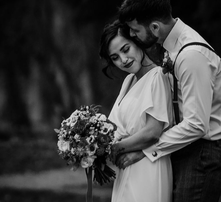 Bride and Groom embrace with red carnation bouquet