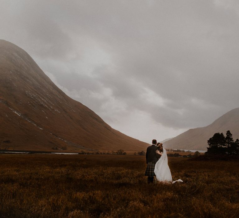 Bride and groom embrace looking out to the Scottish highlands in Glencoe