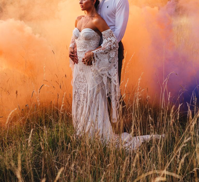 Bride & groom embrace in front colourful smoke bomb in field