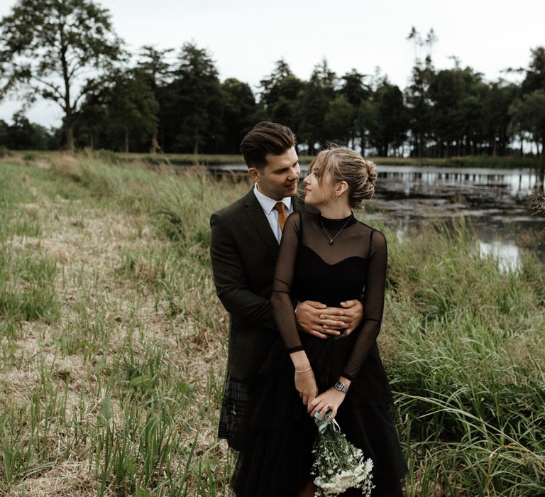 Bride & groom stand in fields wearing black 