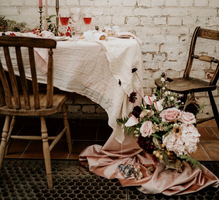 Sweetheart table next to an exposed brick wall dressed with taper candles and natural linens 