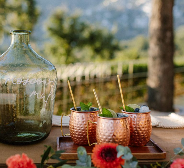 Metal cups filled with cocktails next to large glass vessels with the words 'prosecco' written on them