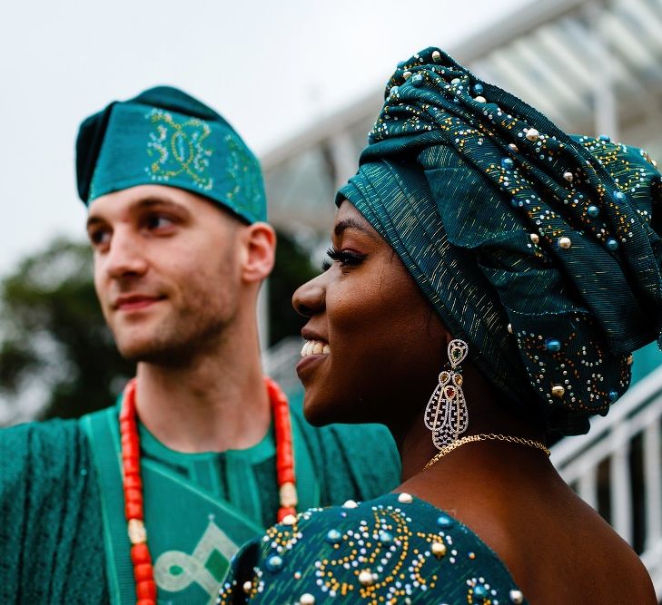 A Black bride wears traditional dress to the evening of her wedding. She has a large headdress on. 