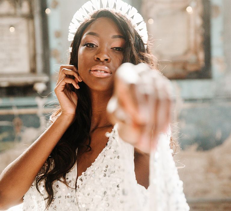 A Black bride points towards the camera and wears a bridal crown.