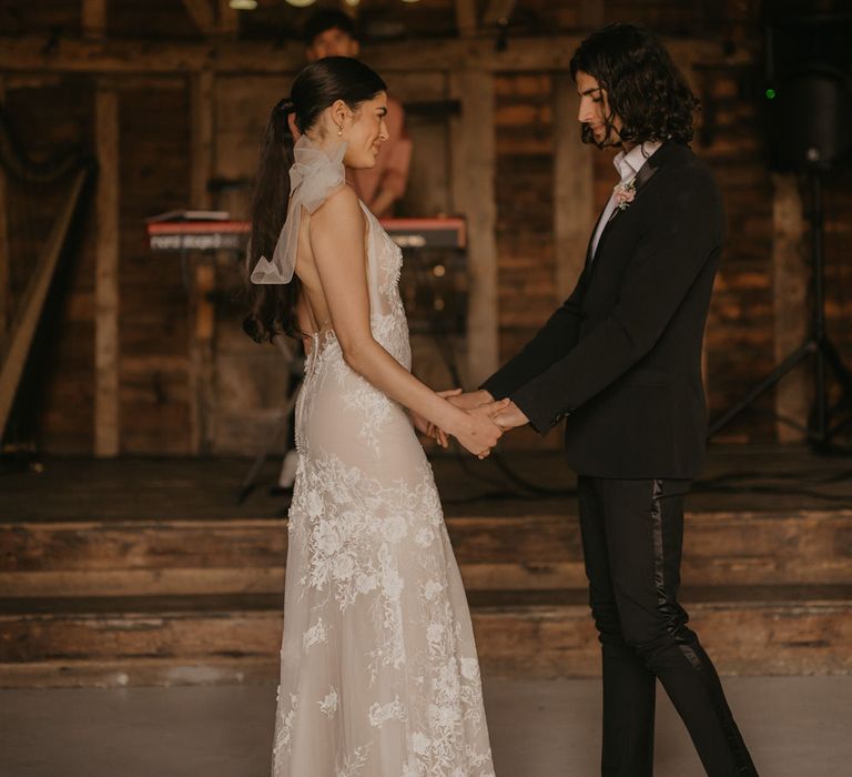 First dance with bride in a fitted lace wedding dress with love back and groom in a black tuxedo with open shirt 