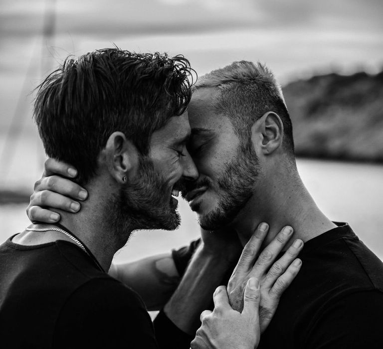 Grooms hold one another as they go to kiss during engagement session