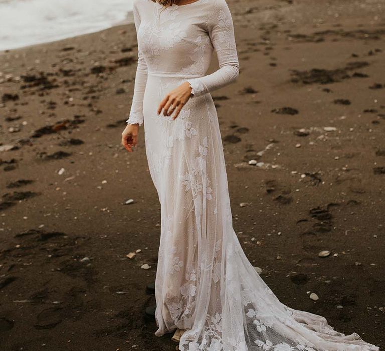 Boho bride in a fitted wedding dress with long sleeves and appliqué detail wearing a fedora hat on the beach in Devon