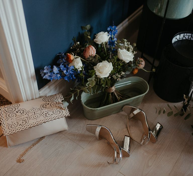 Silver wedding heels with bouquets of blue, orange and white florals including roses, eucalyptus and wild flowers