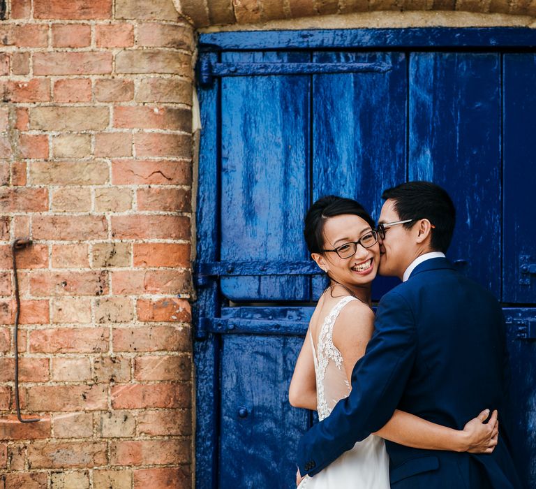 Bride & groom embrace in front of bright blue door on wedding day