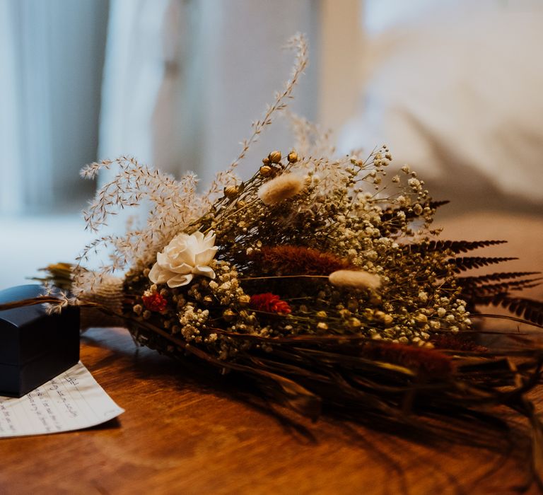 Dried floral bouquet lays upon table next to box and handwritten letter