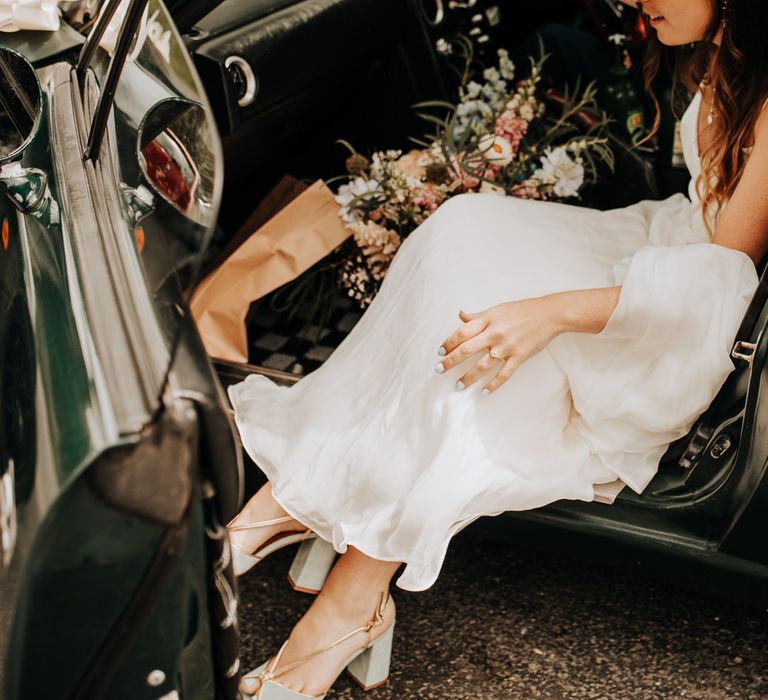 Bride in white cami dress and light blue block heels gets out of green Mazda holding multi coloured bridal bouquet 