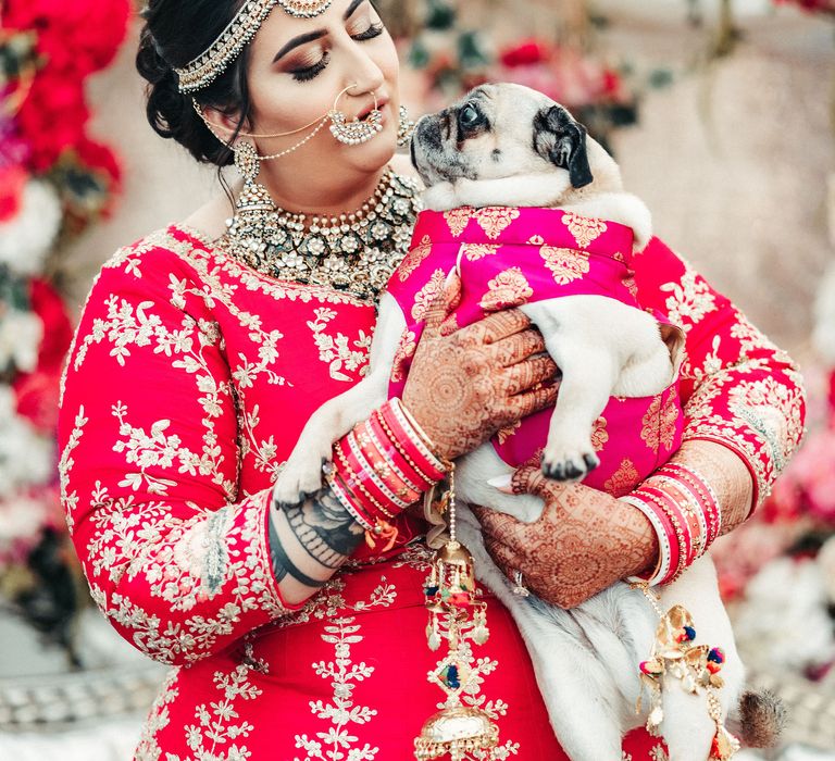 Bride picks up her pug on the day of her wedding whilst wearing pink and gold wedding outfit