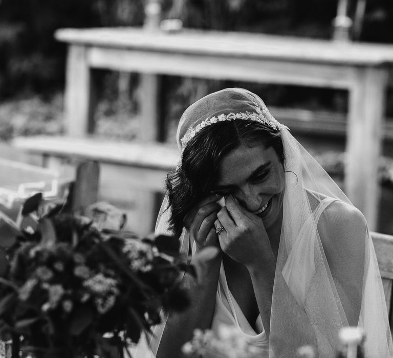 Bride in a lace cap Juliet wedding veil wiping her tears during the intimate pub wedding reception 