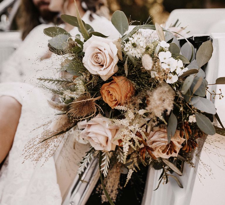 Boho wedding bouquet with orange and cafe au lait roses, foliage and dried grasses 