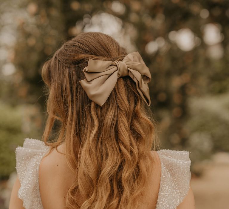 Bride in a sparkly wedding dress with a half up half down wedding hairstyle with satin bow hair accessory 