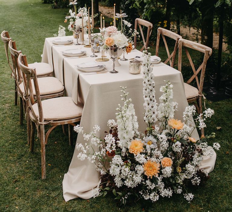 Outdoor wedding reception table decor with natural linen, taper candles, romantic floral arrangements and chandelier light installation