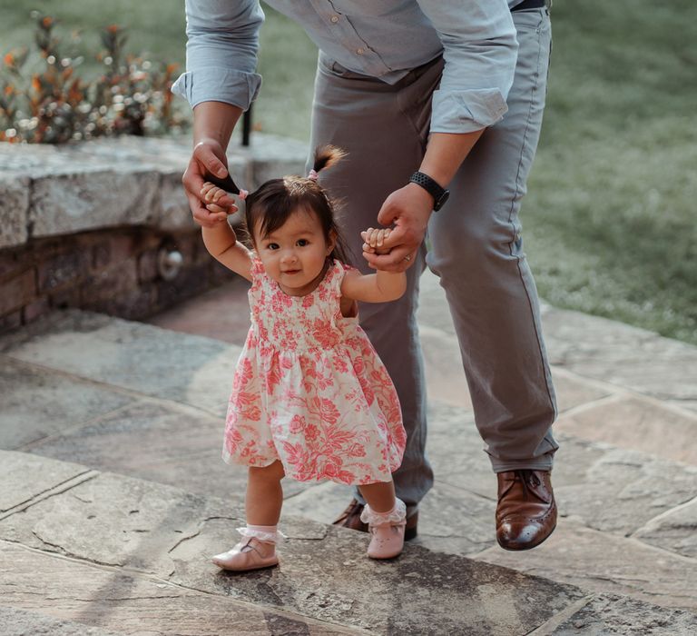 Wedding guests in blue shirt and grey jeans helps young wedding guest in pink and white dress and pink shoes up steps at Wasing Park wedding