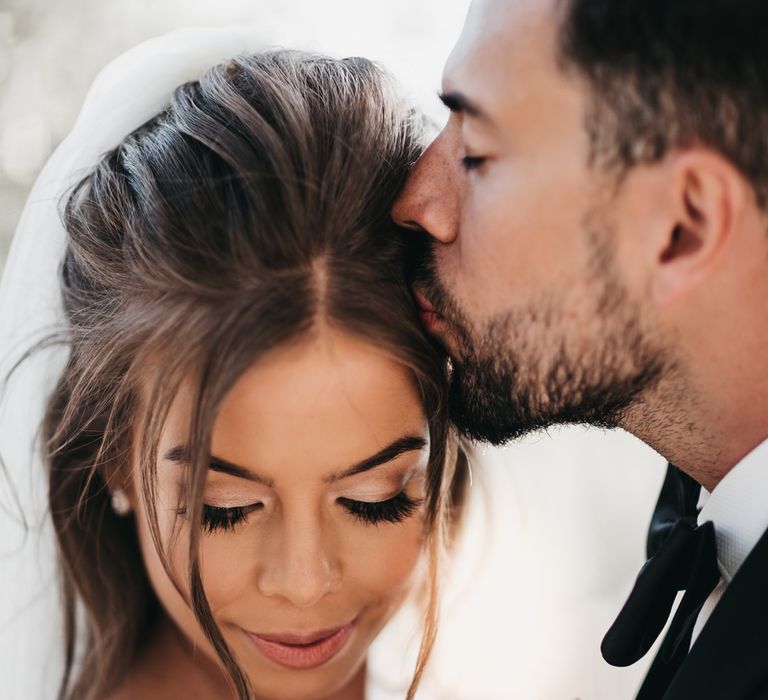 Groom kissing his brides head with shimmering eyeshadow and long extension lashes 