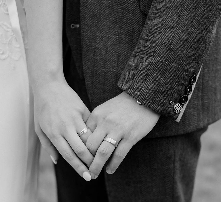 Black & white image of bride and groom holding hands whilst wearing wedding bands after ceremony