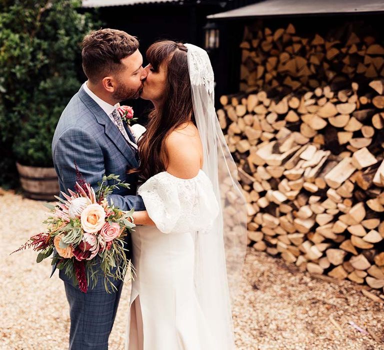 Bride & groom kiss on their wedding day as bride holds floral bouquet