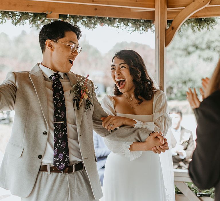 Bride & groom laugh and hold hands during wedding ceremony outdoors