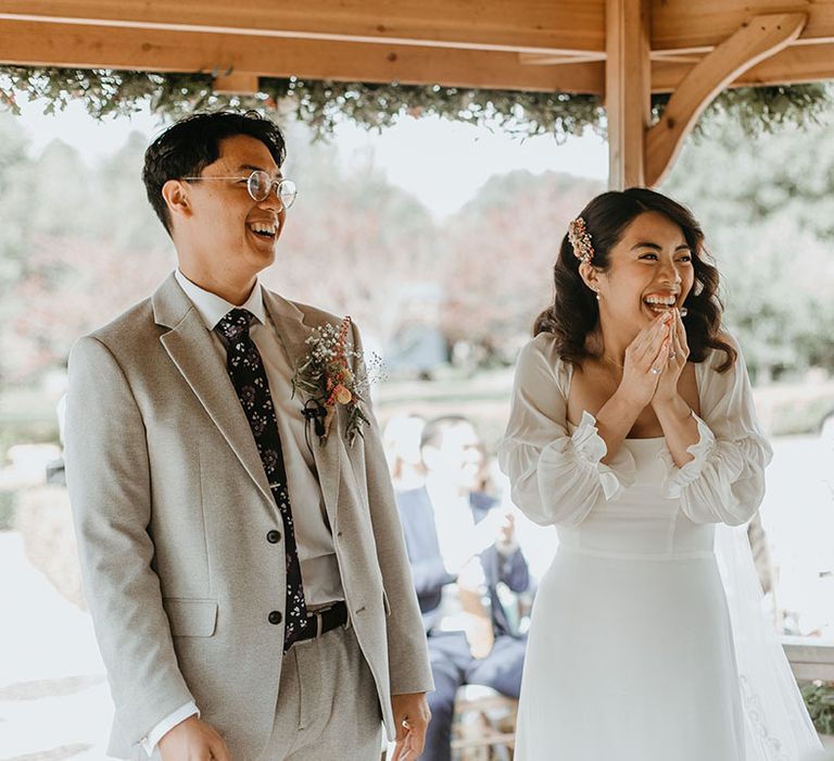 Bride & groom laugh during wedding ceremony under pergola at the Secret Garden Wedding venue