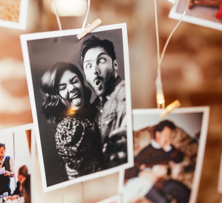 Black and white photo of bride and groom on wedding photo wall with fairy lights for rustic barn wedding reception 