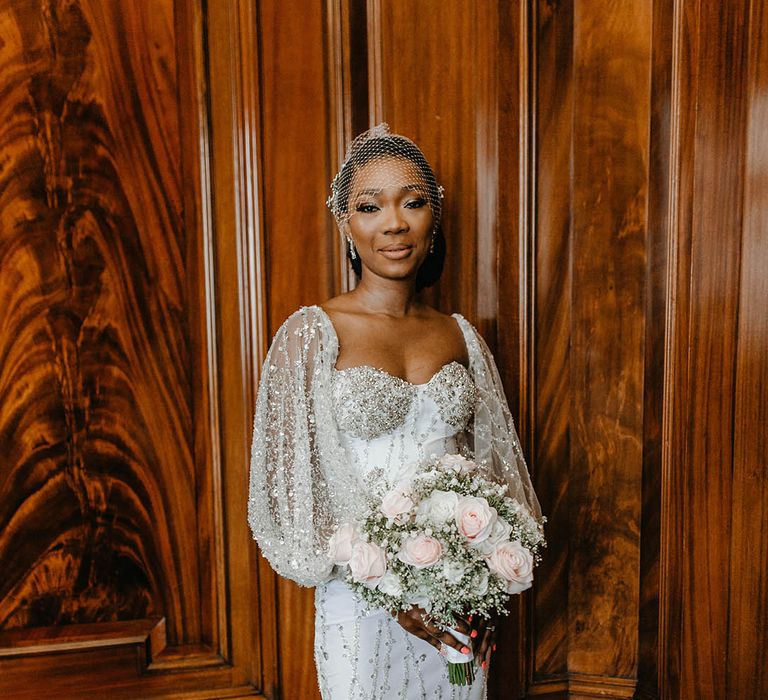 Bride wears sequin embellished wedding gown complete with full sleeves and holds classic floral bouquet