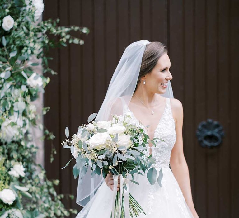 Bride in a Martina Liana Bridal wedding dress and veil holding a white rose and eucalyptus wedding bouquet 