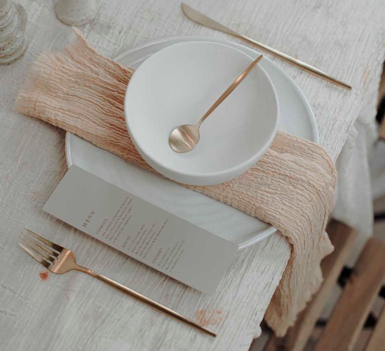 minimalist place setting with charger plate, bowl, linen napkin, menu card and gold cutlery 