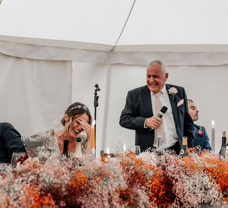 Bride and groom laughing during the wedding speeches with coloured gypsophila cloud top table wedding flowers 