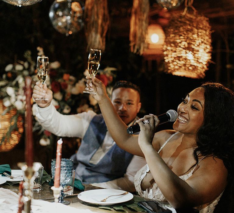 Bride holds a toast at the wedding reception in Tulum with disco ball and wooden lanterns