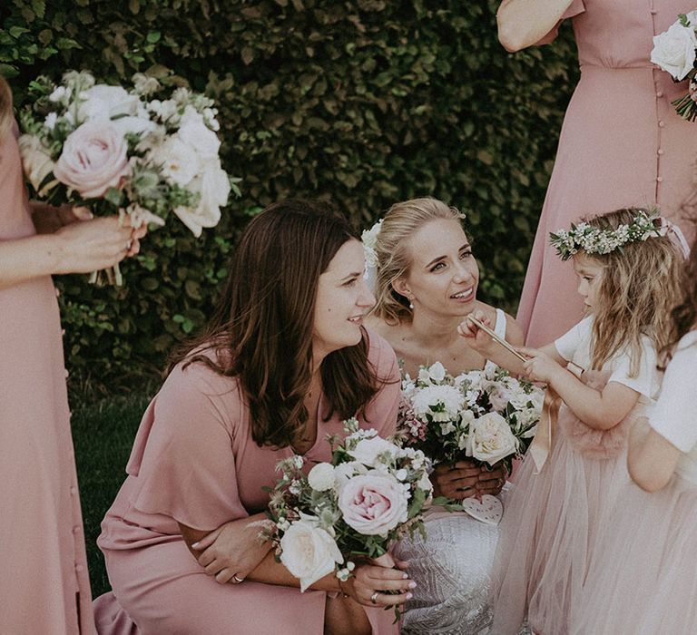 Bride and bridesmaids talk to flower girls in flower crowns and pink and white dresses with bows and ribbons