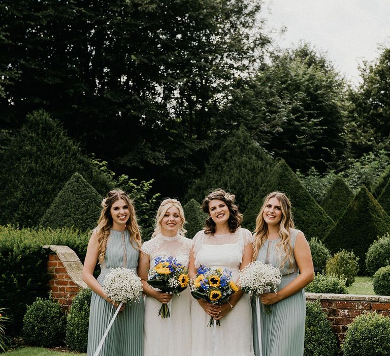 Brides pose with their bridesmaids in green pleated dresses on their wedding day