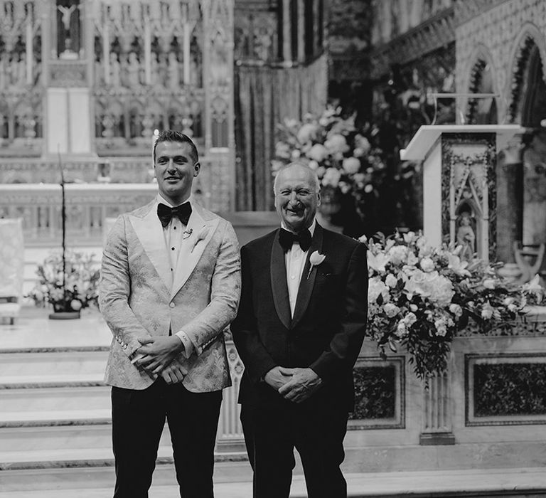 Groom and groomsman in black tie smile as they ge their first look at the bride as she enters their London city venue